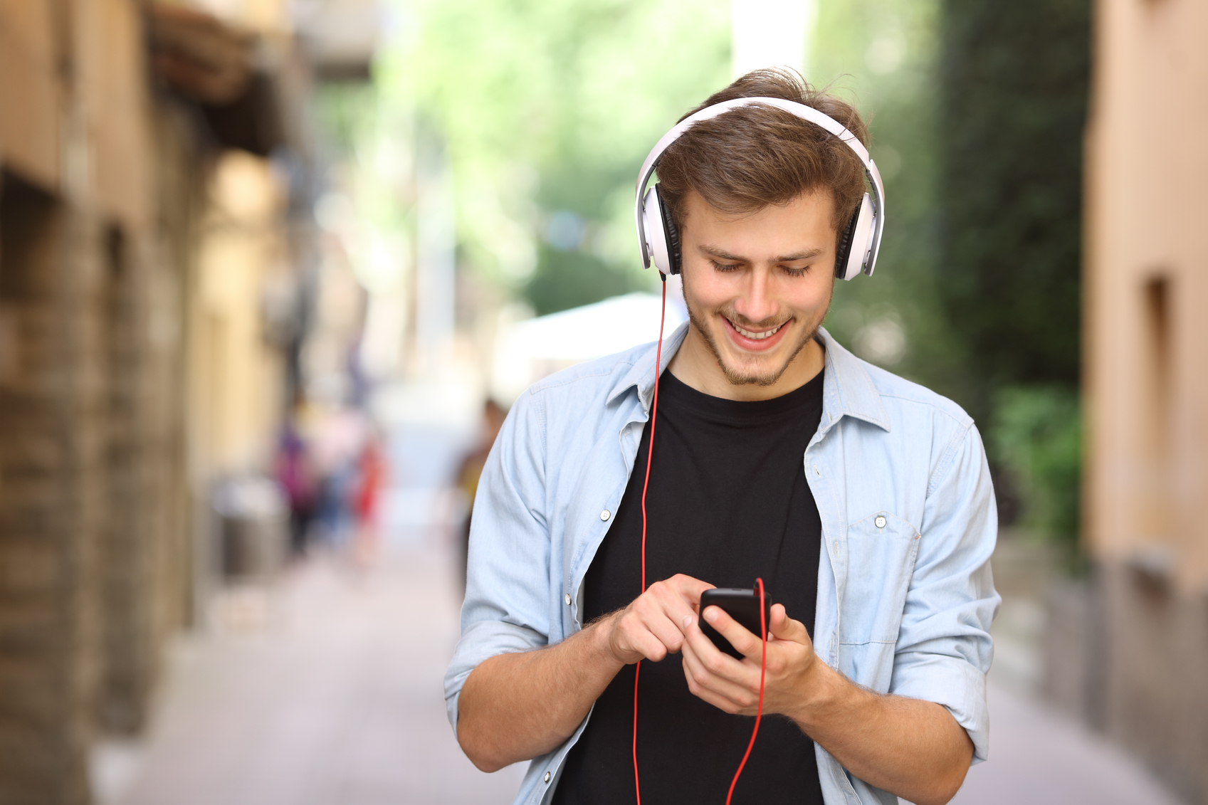 Happy guy walking and using a smart phone to listen music with headphones