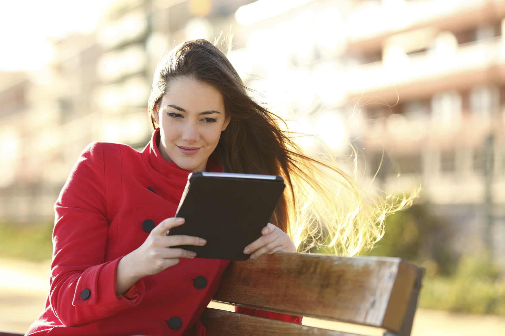 Woman reading an ebook or tablet in an urban park with buildings in the background