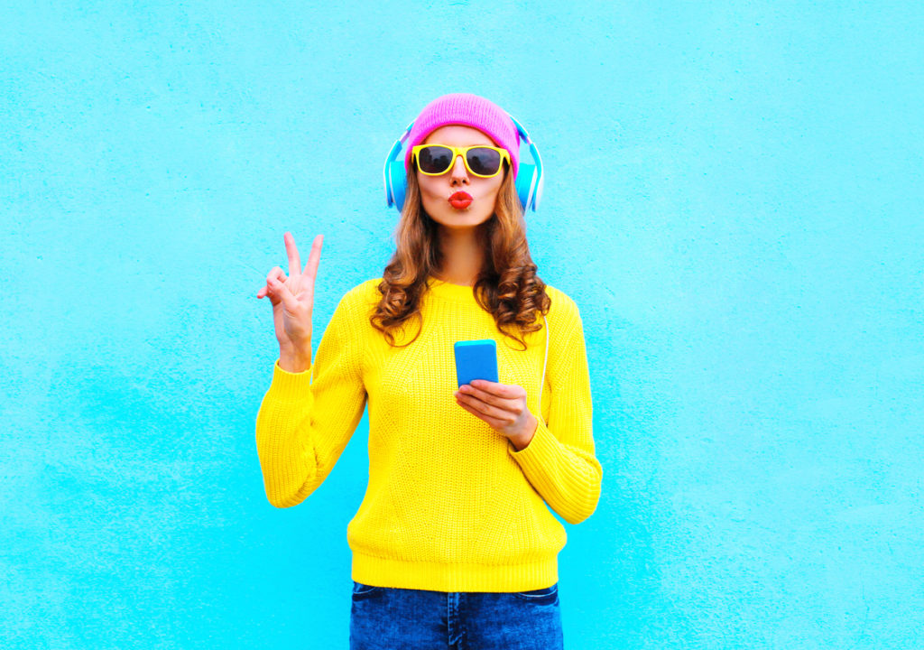 Fashion pretty woman listening music in headphones with smartphone colorful
