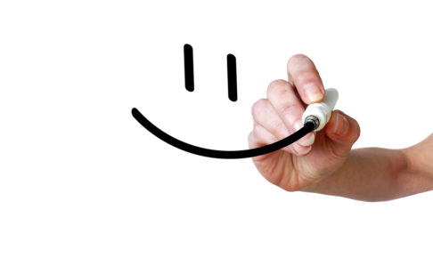 Hand draws smiley with black marker on transparent whiteboard