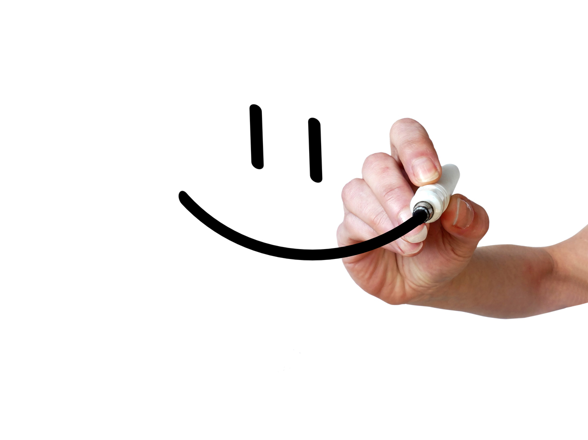 Hand draws smiley with black marker on transparent whiteboard