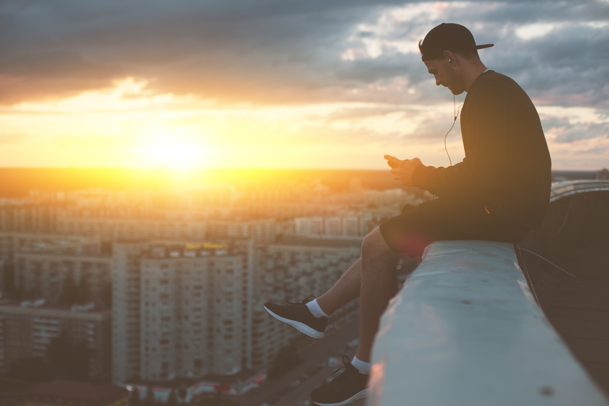 Man sitting on the edge of the roof with smartphone