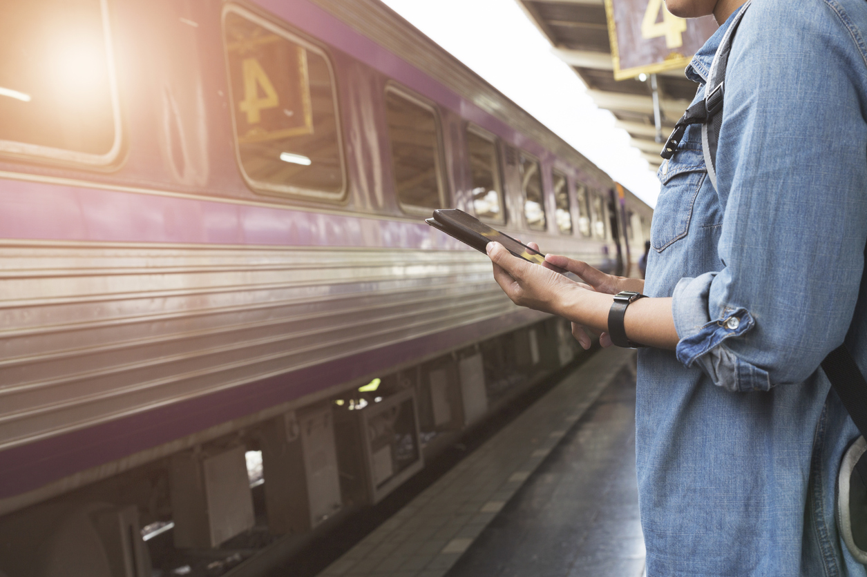 woman holding smartphone with backpack at train station