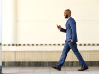 Side portrait of young african business man walking with mobile phone