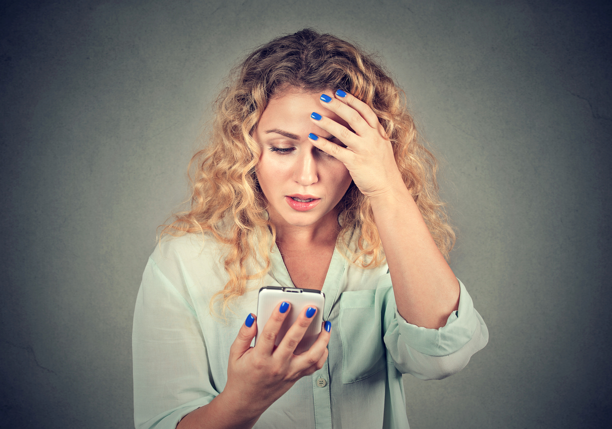 Upset stressed woman holding cellphone disgusted with message she received