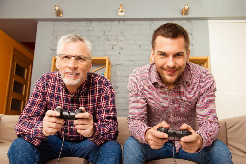 Happy man and his father playing video games while sitting on sofa