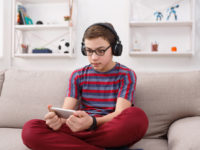 Excited teenage boy playing mobile game at home