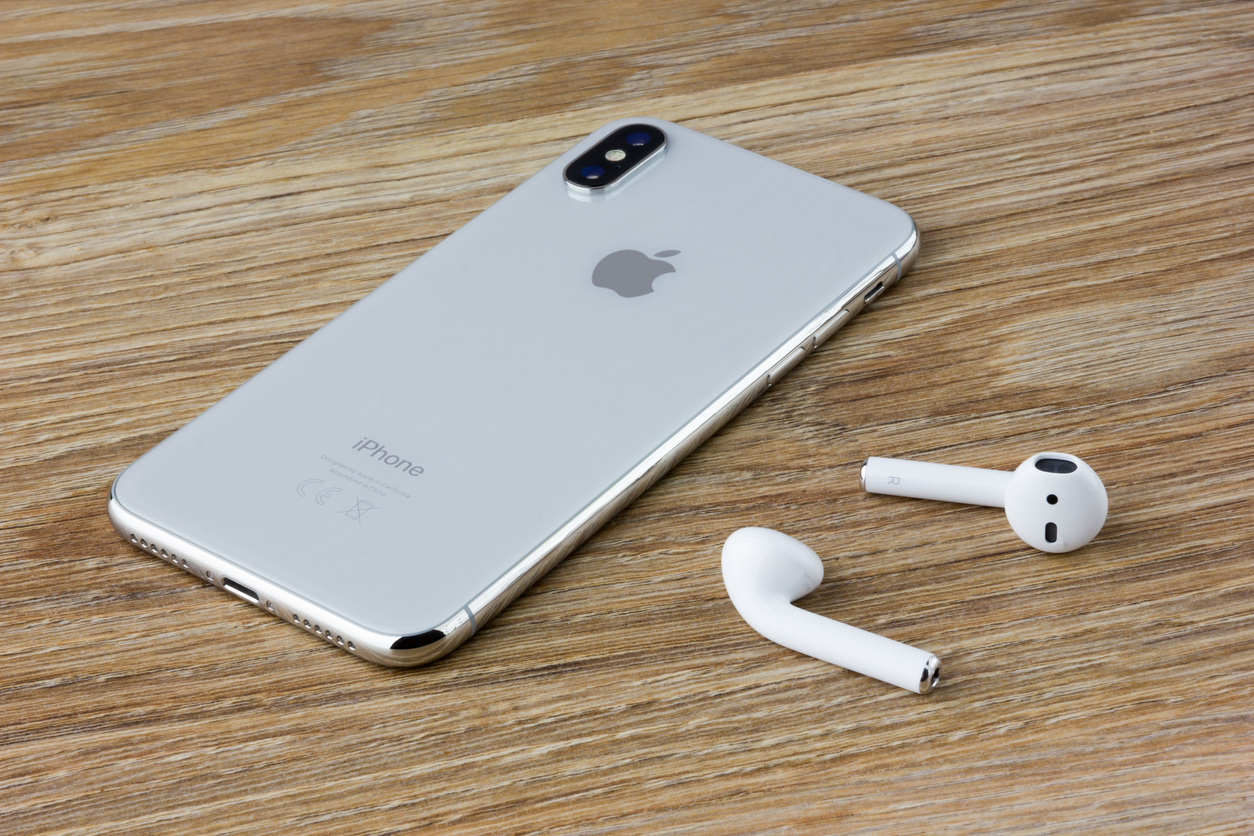 The Iphone 10 lies on a wooden table next to the wireless headphones airpods from the Apple.