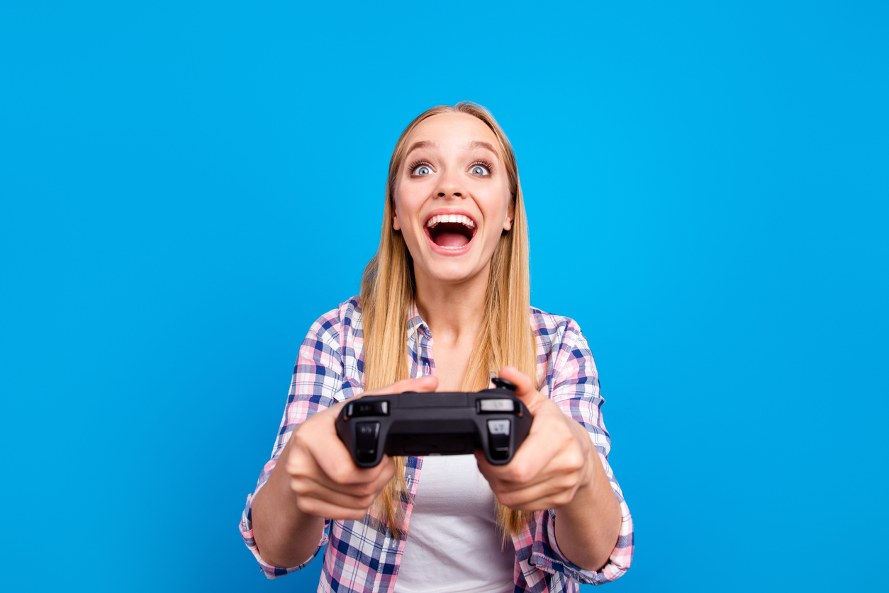 Close up of happy young blond girl holding joystick in hands and play in video games isoletad on blue background. Concept of victory and loses, competition and match