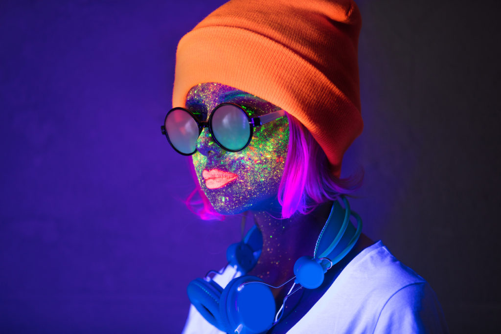 Young girl in hat with fluorescent paint on lips and face and headphones. Studio shot.