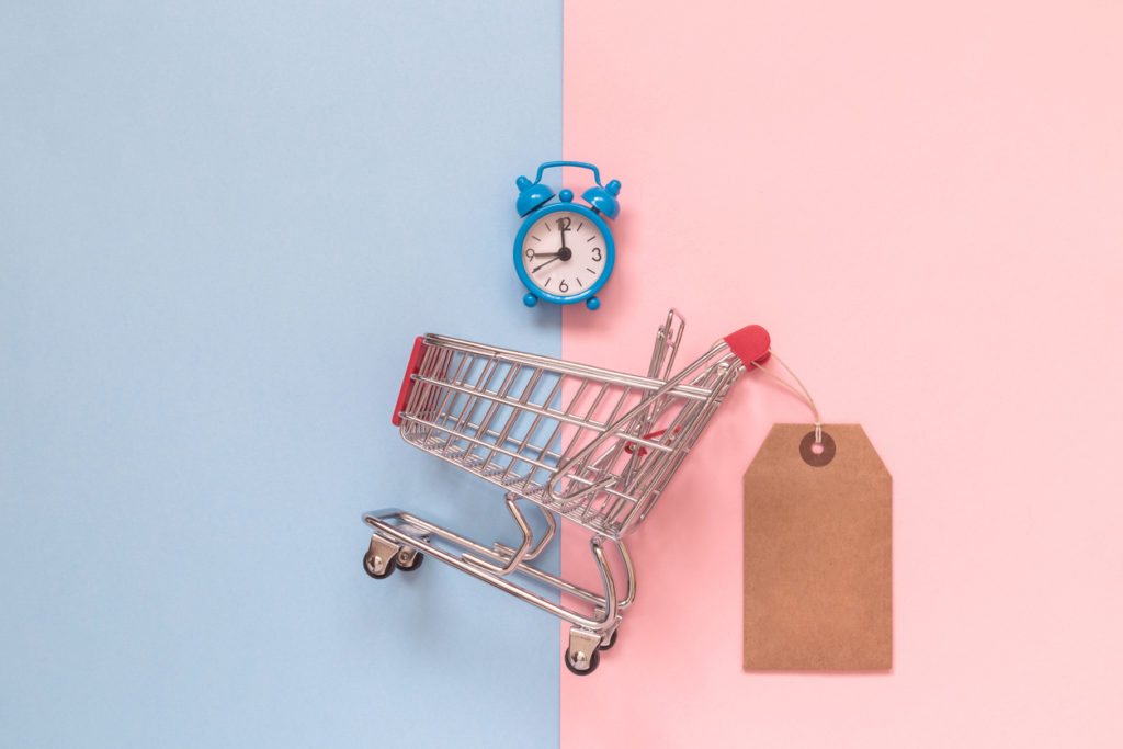 Small shopping cart with blank price tag and alarm clock on pastel background minimal creative concept