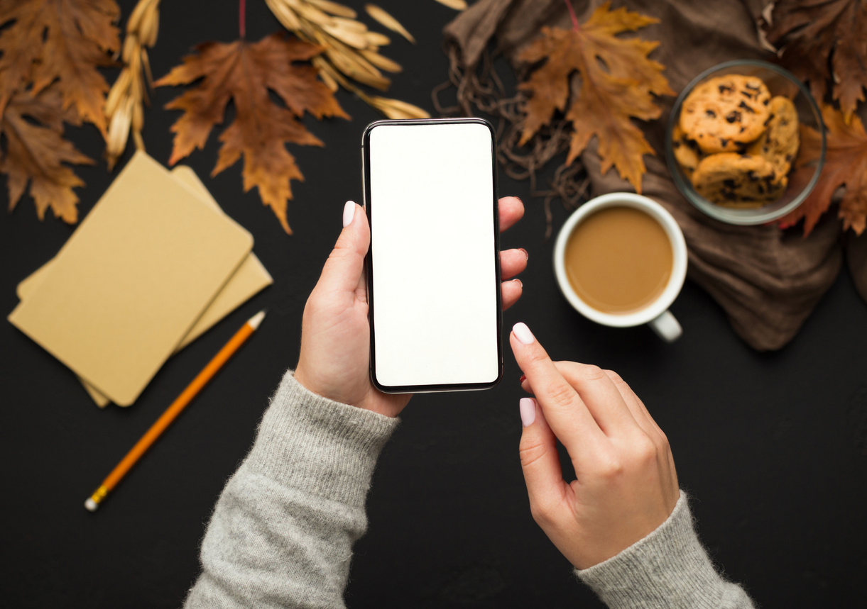 Woman holding cellphone with blank screen over autumn background
