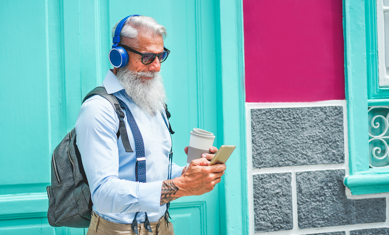 Trendy senior man using music smartphone app and drinking coffee in downtown center outdoor - Mature fashion male having fun with new trends technology - Tech and joyful elderly lifestyle concept