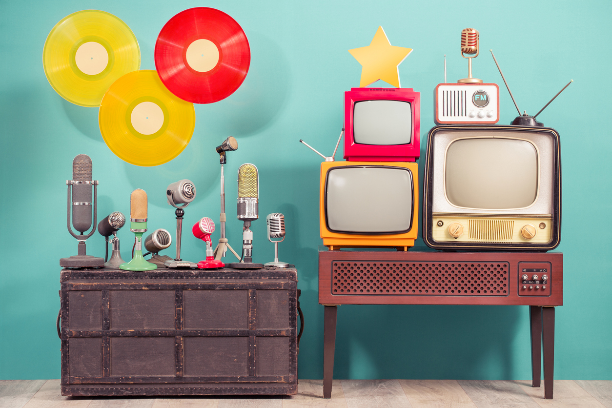 Retro studio microphones, outdated TV set, old FM radio, golden award star, flying multicolor LP vinyl record discs front blue background. Nostalgia music and journalism concept. Vintage style photo