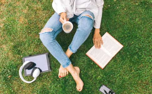 Young woman sitting on the grass drinking coffee and reading a book enjoys outdoor recreation.