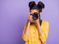 Photo of amazing dark skin lady holding photo digicam in hands photographing foreign sightseeing abroad wear yellow shirt trousers isolated purple color background