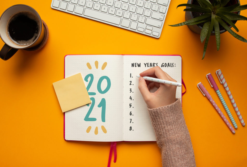 Stock photo of woman writing goals in a 2021 new year notebook on yellow background