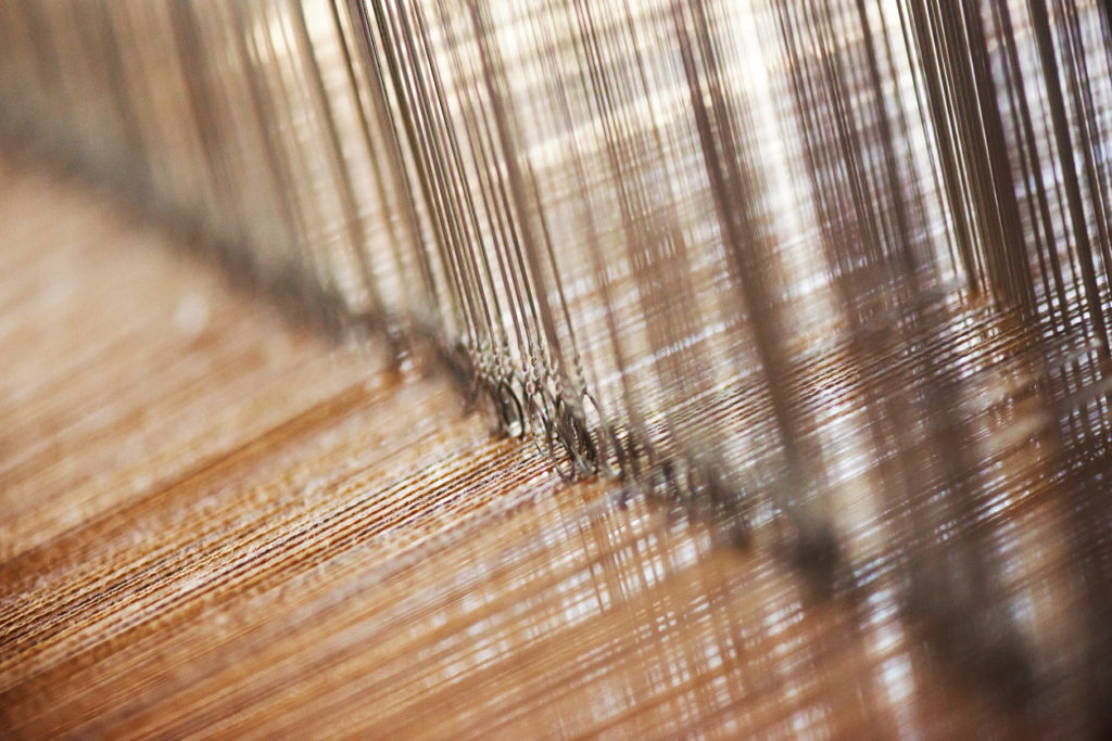Close-up of the cotton yarn which is being woven by a loom