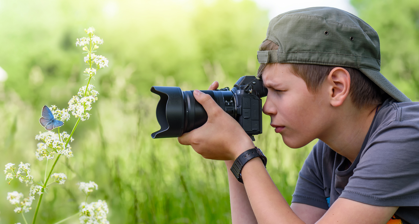 Boy holding digital camera and shooting butterfly on the wild flower